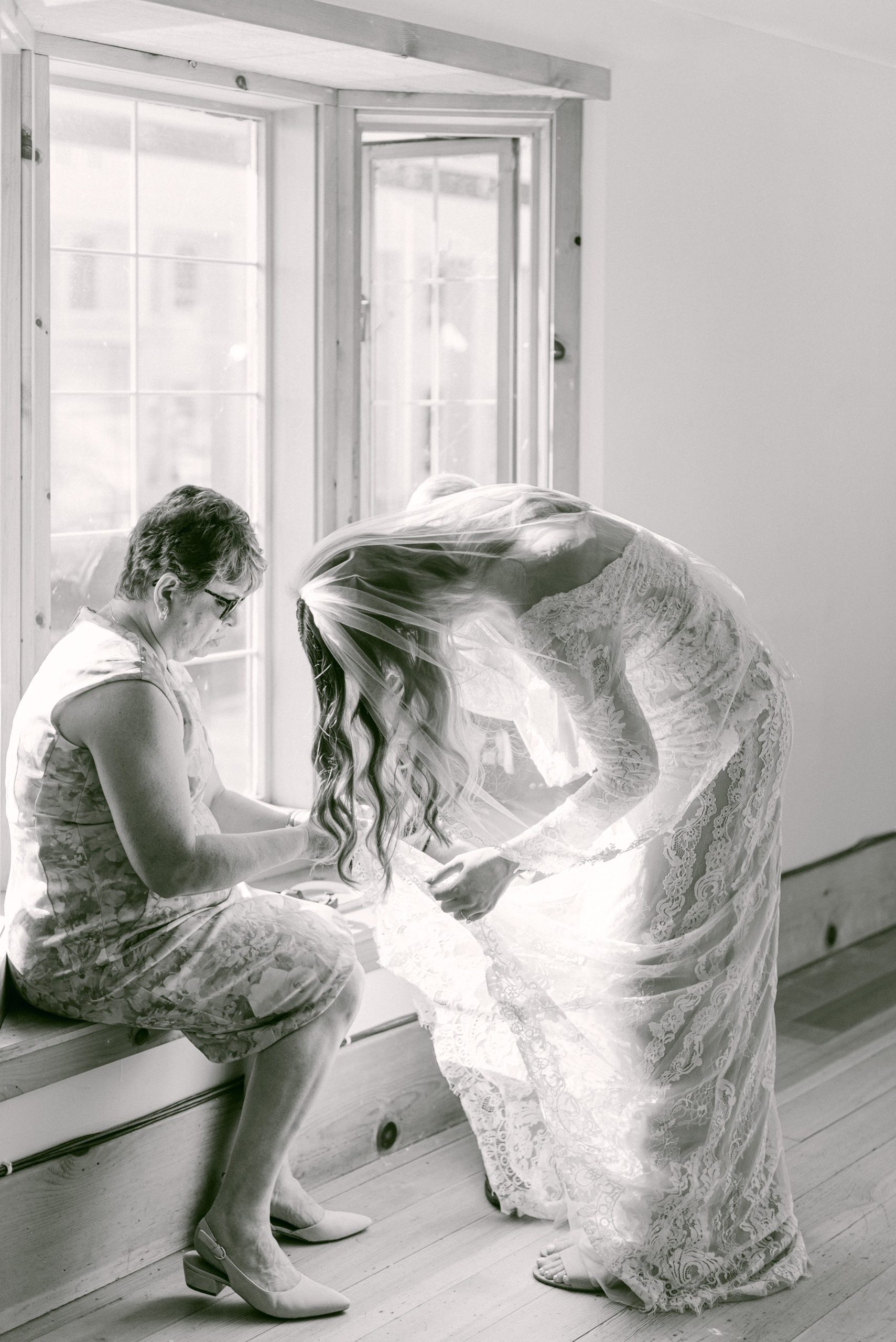 Fine Art Weddings in Seattle, Washington. The Sound Hotel, and The Center for Wooden Boats. Mother of the bride fixing bride's dress snag in the sunny window seat before the wedding ceremony.